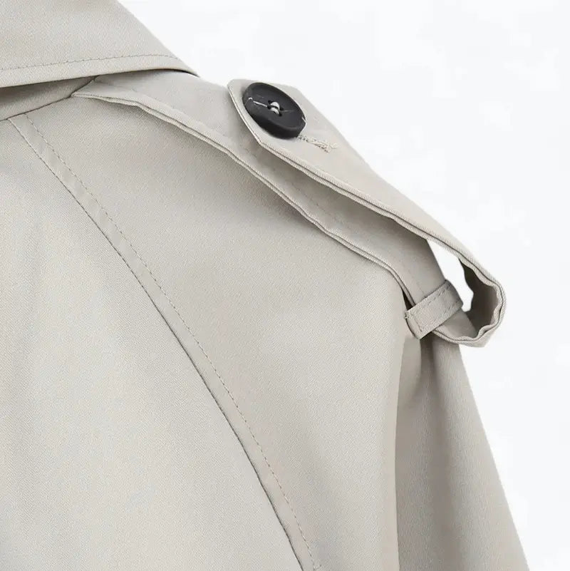 Close-up da alça de ombro e gola da jaqueta feminina cropped cinza estilo trench coat, com botão preto.