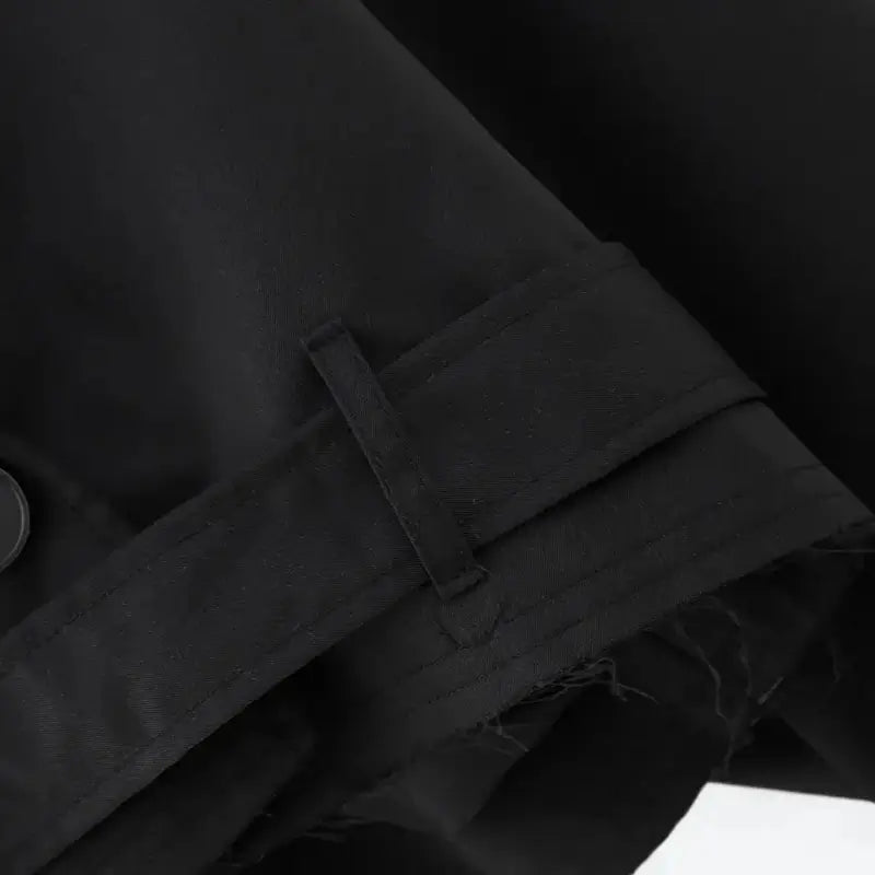 Close-up da barra da jaqueta feminina cropped preta estilo trench coat, detalhando o cinto ajustável com presilhas e o acabamento levemente desfiado.