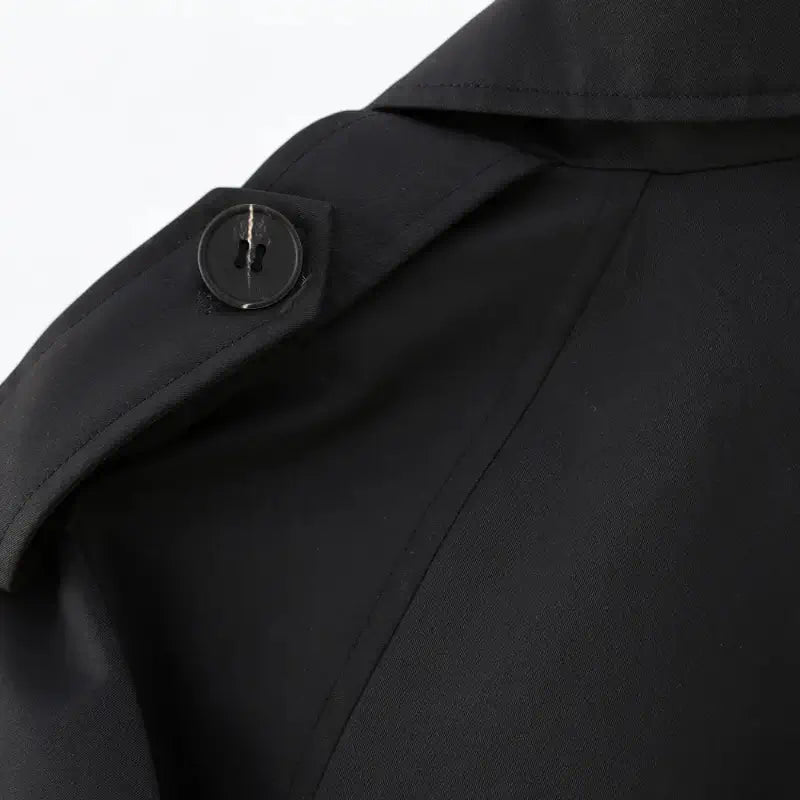 Close-up da alça de ombro da jaqueta feminina cropped preta estilo trench coat, com botão preto e costura da manga.