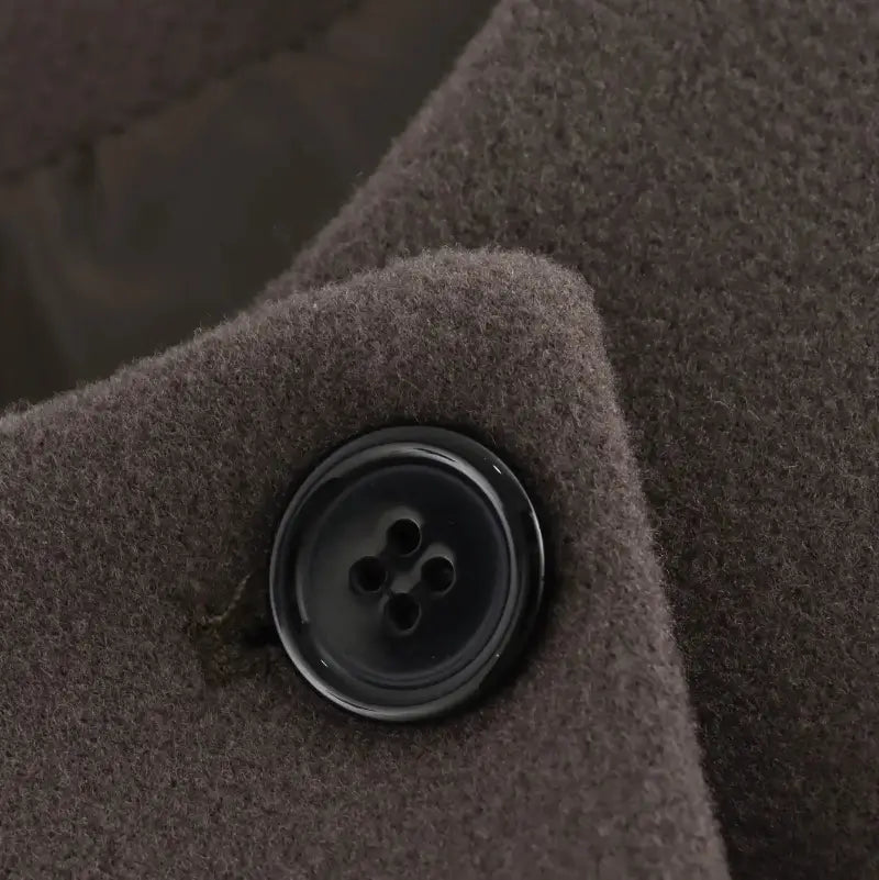 Detalhe ampliado do botão preto redondo, costurado na jaqueta feminina marrom, exibindo a textura do tecido.