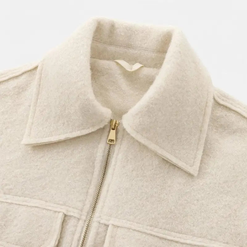 Close-up da gola de camisa e zíper dourado da jaqueta feminina off-white, destacando a textura felpuda do tecido.