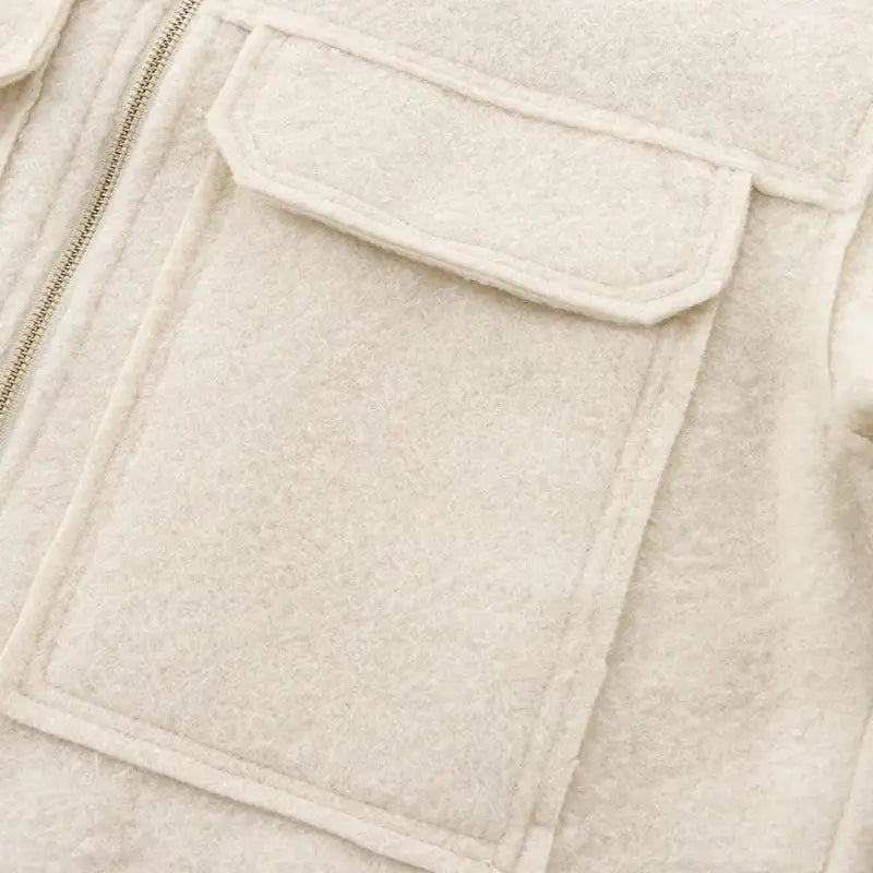 Close-up do bolso chapado com lapela da jaqueta feminina off-white, exibindo a textura de lã do tecido e parte do zíper dourado.