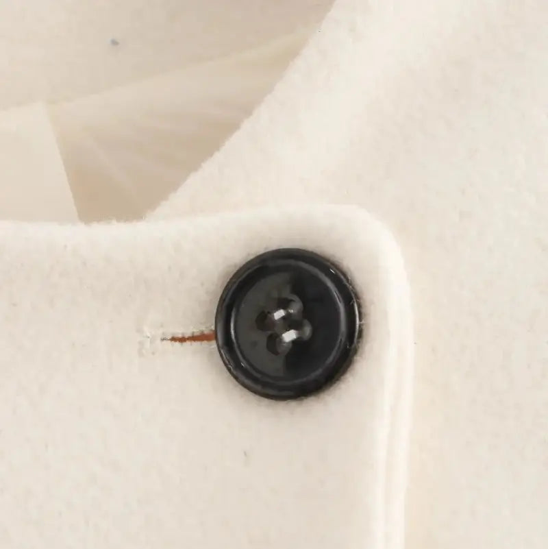 Detalhe ampliado do botão preto redondo, costurado na jaqueta feminina off-white, exibindo a textura do tecido.