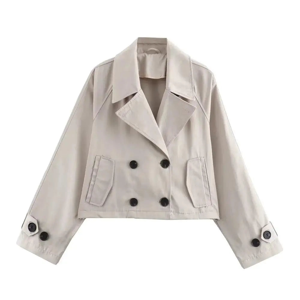 Jaqueta feminina cropped bege estilo trench coat, com lapelas, abotoamento duplo por botões pretos contrastantes, e bolsos chapados, exibida em fundo branco.