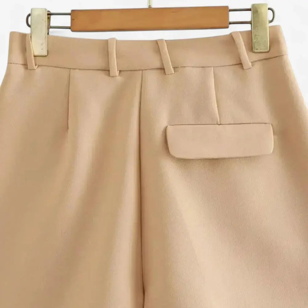 Vista traseira do short alfaiataria feminino bege, de cintura alta, com presilhas de cinto e detalhe de bolso com aba na parte posterior.