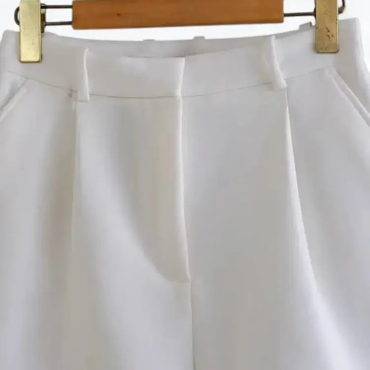 Short alfaiataria feminino branco, modelo cintura alta com pregas frontais bem marcadas e bolsos laterais discretos, pendurado em cabide de madeira.