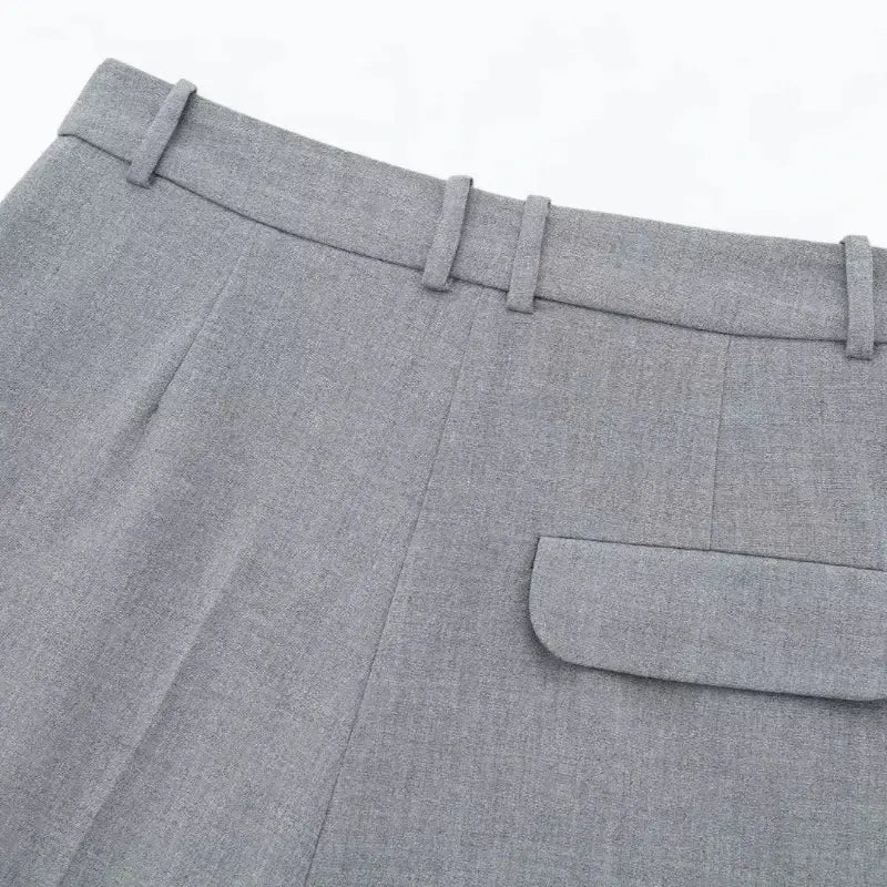 Close-up da cintura traseira do short feminino de alfaiataria cinza, com presilhas de cinto e detalhe do bolso com lapela.