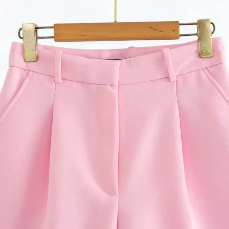 Short alfaiataria feminino rosa, modelo cintura alta com pregas frontais bem marcadas e bolsos laterais discretos, pendurado em cabide de madeira.