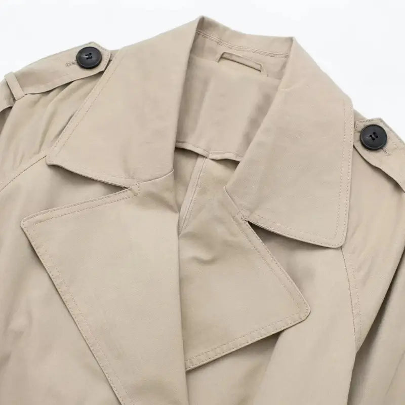 Close-up da gola, lapelas e ombros do sobretudo feminino bege estilo trench coat, destacando os botões pretos.