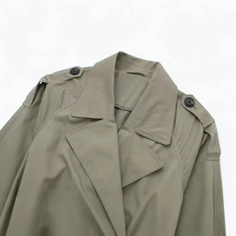 Close-up da gola, lapelas e ombros do sobretudo feminino verde estilo trench coat, destacando os botões pretos.