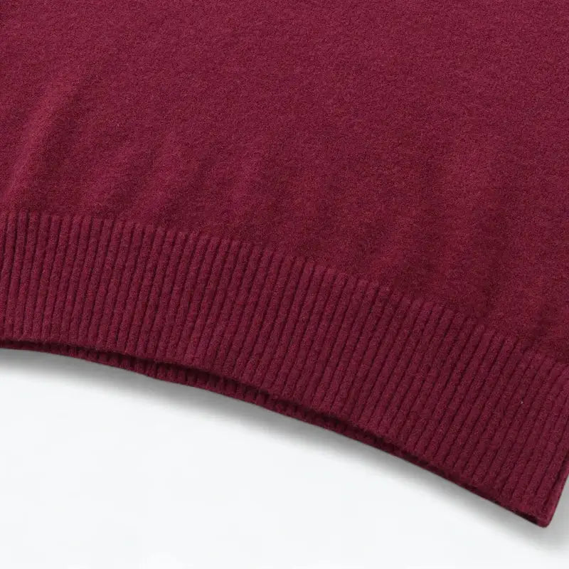 Close-up da barra do suéter feminino vermelho, detalhando o acabamento canelado da peça.